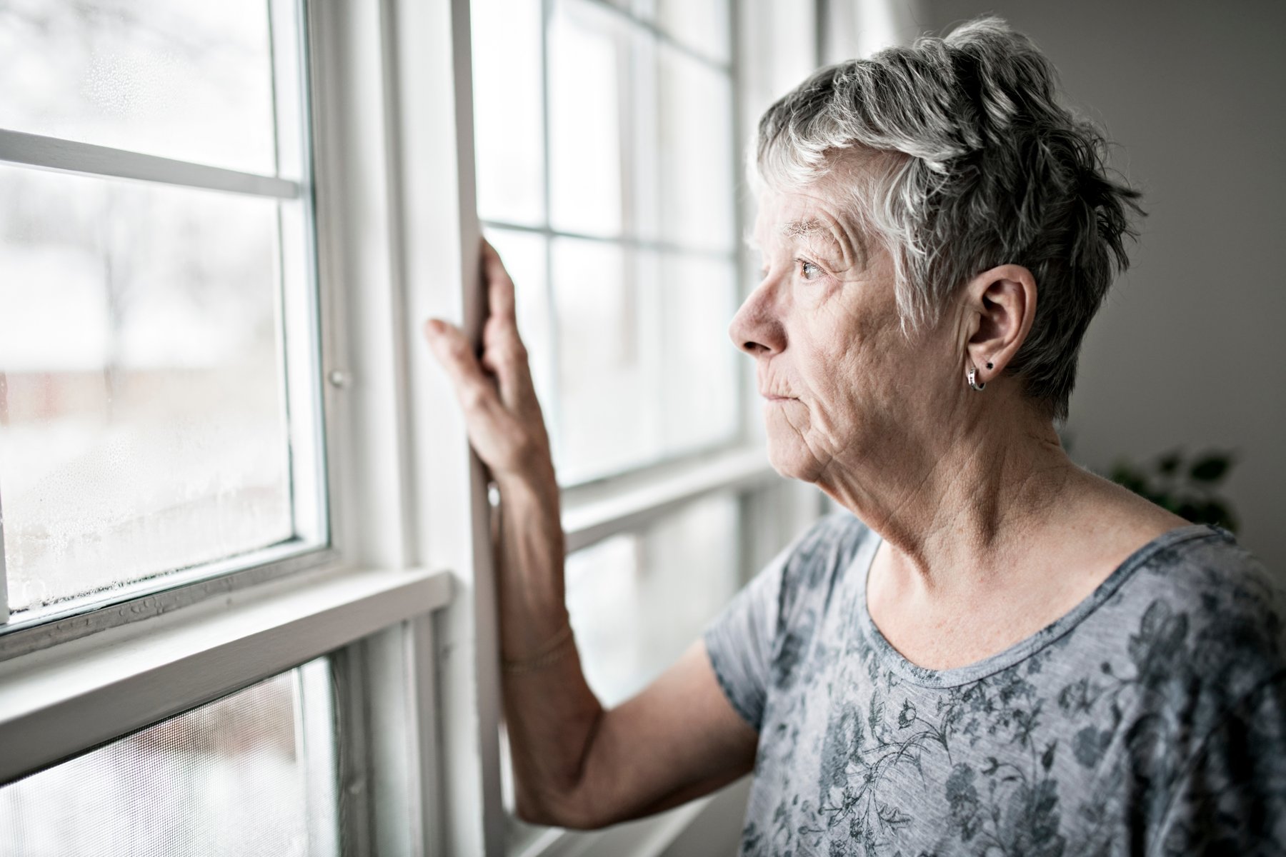 An older adult looking thoughtfully out a window